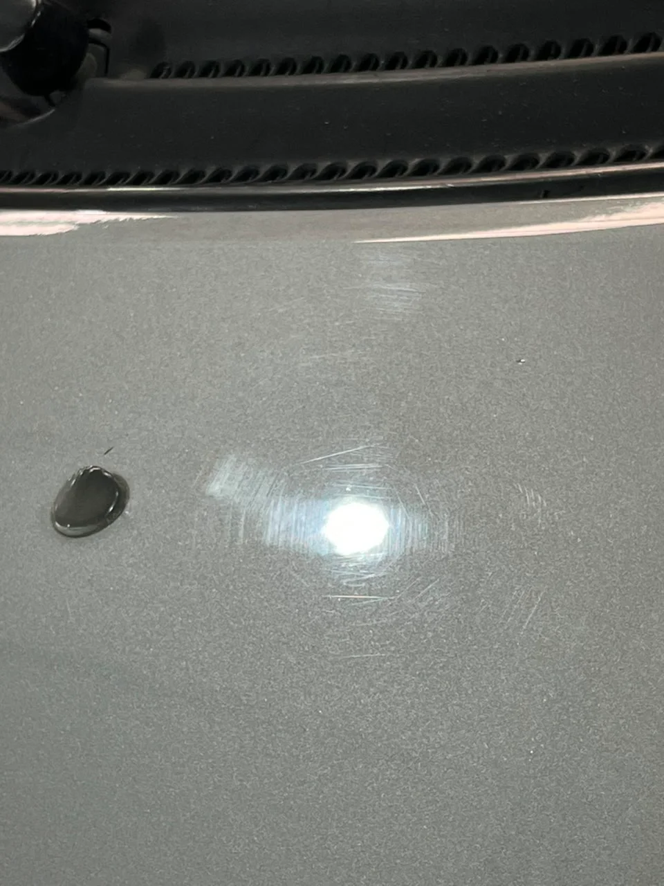 Capó gris bajo la luz: micro-rayones circulares (swirls) alrededor del reflejo